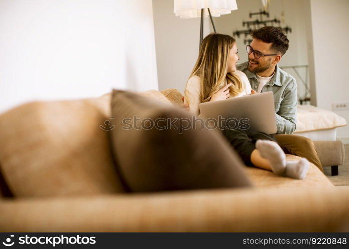 Handsome young couple using laptop together while sitting on sofa at home