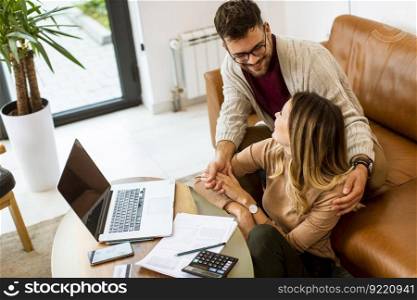 Handsome young couple using laptop together while sitting on sofa at home