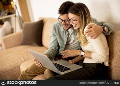 Handsome young couple using laptop together while sitting on sofa at home