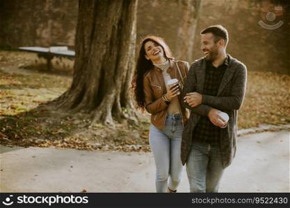 Handsome young couple walking in autumn park with coffee to go cups in hands