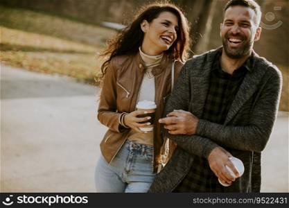 Handsome young couple walking in autumn park with coffee to go cups in hands