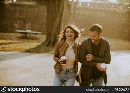 Handsome young couple walking in autumn park with takeaway coffee in hands