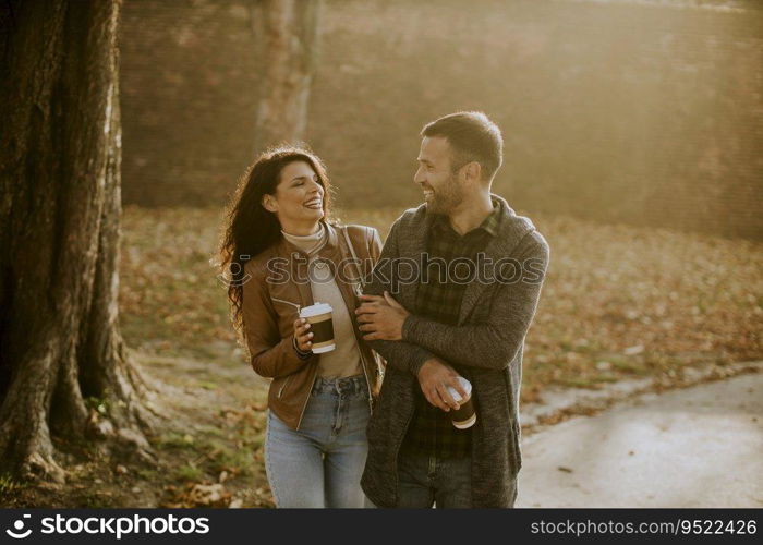 Handsome young couple walking in autumn park with takeaway coffee in hands