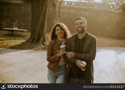 Handsome young couple walking in autumn park with takeaway coffee in hands