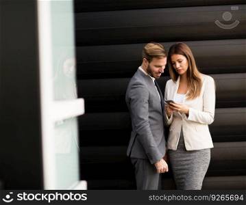 Handsome young couple with mobile phone in front of office building