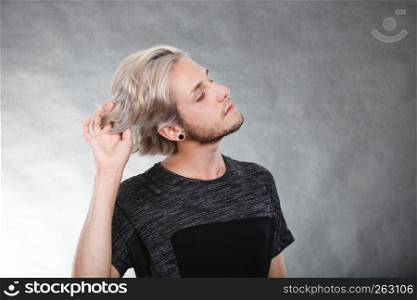 Handsome young fashion model with colored hair highlighted stylish haircut, ear plug, side view. Portrait young man with stylish haircut