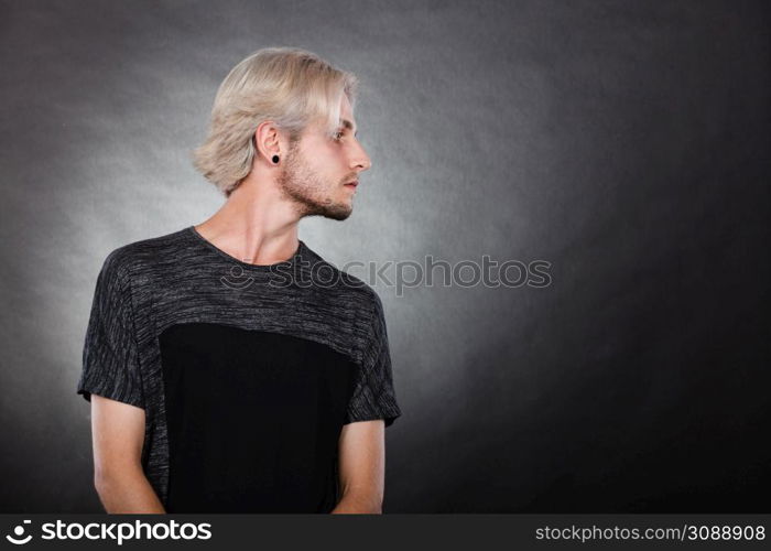 Handsome young fashion model with colored hair highlighted stylish haircut, ear plug, side view. Portrait young man with stylish haircut