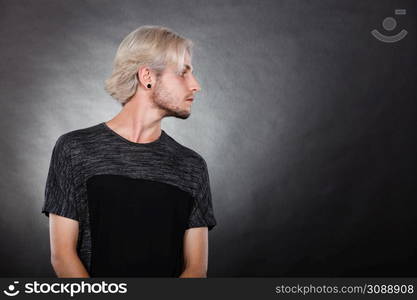 Handsome young fashion model with colored hair highlighted stylish haircut, ear plug, side view. Portrait young man with stylish haircut