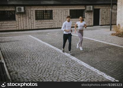 Handsome young fitness couple running in urban area