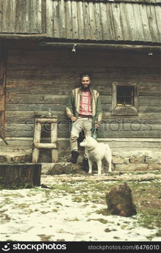 handsome young hipster man standing together with white husky dog in front of old vintage retro wooden house. hipster with dog in front of wooden house