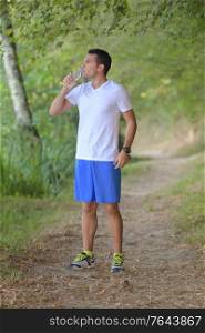 handsome young man athlete drinking water in forest
