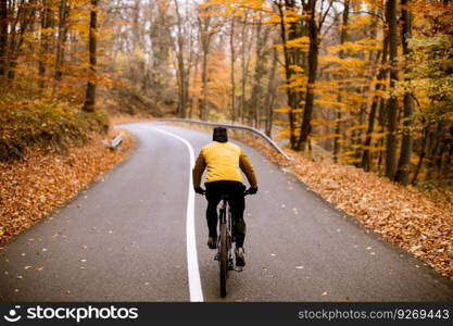 Handsome young man biking on a country road through autumn forest