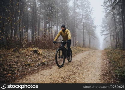 Handsome young man biking through autumn forest