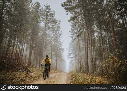 Handsome young man biking through autumn forest
