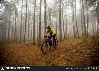 Handsome young man biking through autumn forest