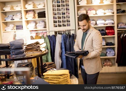 Handsome young man buying trousers in the store