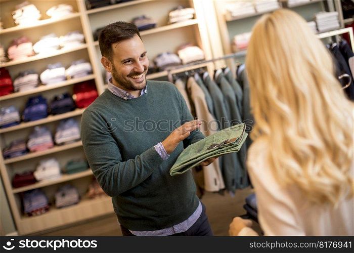 Handsome young man buying trousers with his wife in the store
