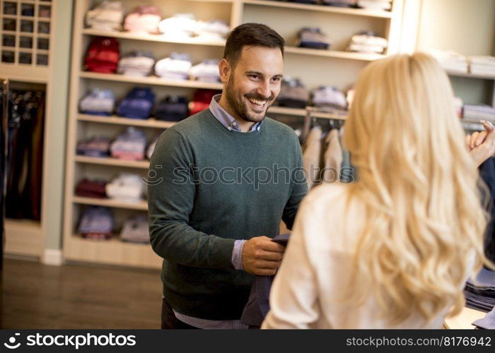 Handsome young man buying trousers with his wife in the store