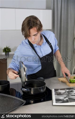 Handsome young man checking a pot at a kitchen on an out of focus background. Safety and cooking at home concept.po. Handsome young man checking a pot at a kitchen