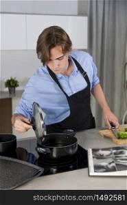 Handsome young man checking a pot at a kitchen on an out of focus background. Safety and cooking at home concept.po. Handsome young man checking a pot at a kitchen