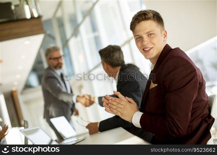 Handsome young man clapping hands after successful business meeting in the modern office