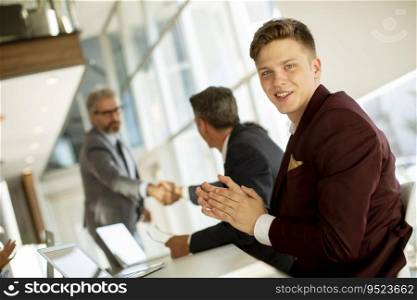 Handsome young man clapping hands after successful business meeting in the modern office