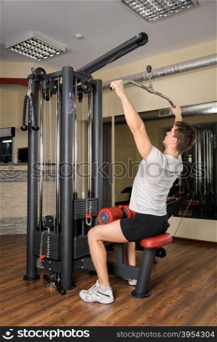 Handsome young man doing B lats pull-down workout in gym