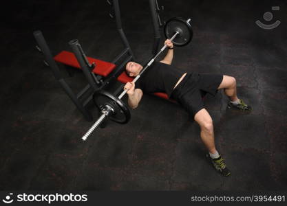 Handsome young man doing bench press workout in gym. Copy space at left lower corner.