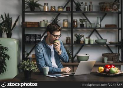 handsome young man eating apple looking digital tablet kitchen