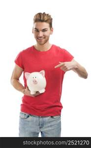 Handsome young man holding and pointing to a piggy bank and smiling