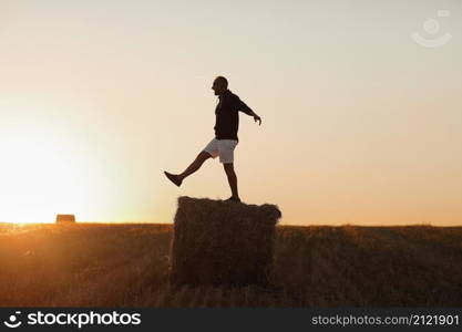 handsome young man in black sweatshirt and white short, in summer field outdoor, having fun on hay bale, haystack on sunset.. handsome young man in black sweatshirt and white short, in summer field outdoor, having fun on hay bale, haystack on sunset