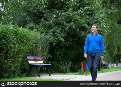 Handsome young man in blue sweater walking in the summer park