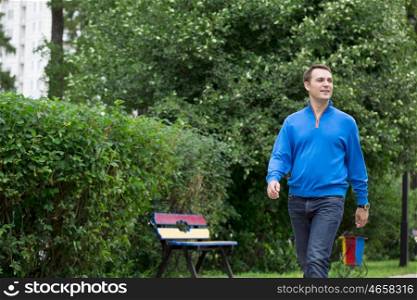 Handsome young man in blue sweater walking in the summer park