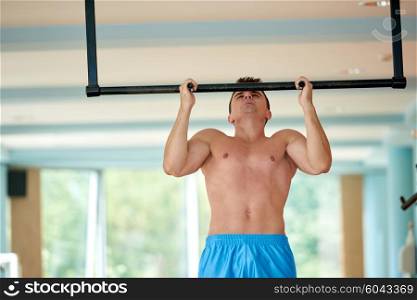 handsome young man in fitness gym lifting up and hanging while working on hands and back muscles