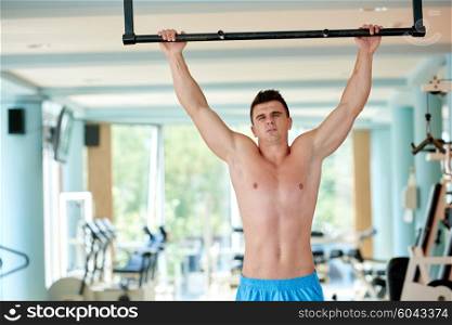 handsome young man in fitness gym lifting up and hanging while working on hands and back muscles