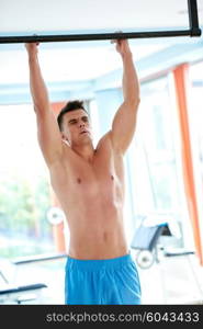 handsome young man in fitness gym lifting up and hanging while working on hands and back muscles