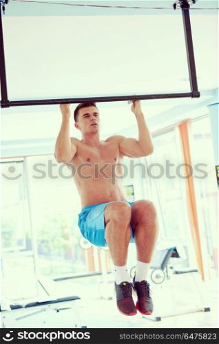 handsome young man in fitness gym lifting up and hanging while working on hands and back muscles. handsome young mand working out in gym