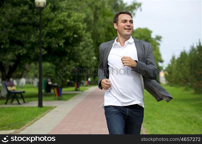 Handsome young man in gray suit walking in the summer park