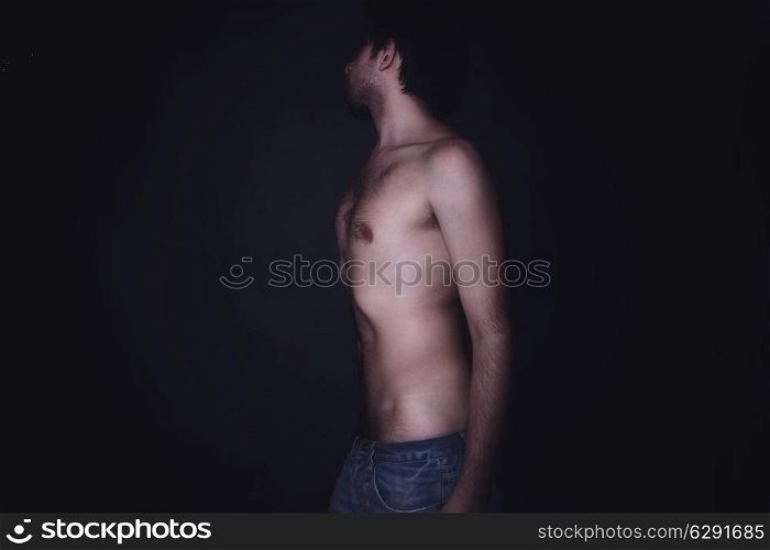 Handsome young man in jeans with bare-chested on a black background