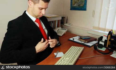 handsome young man in suit, adjusts his clothes and red tie at workplace