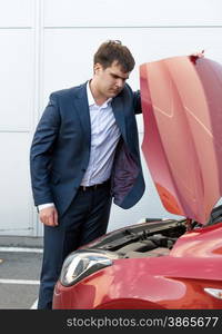 Handsome young man in suit looking under the hood of broken car