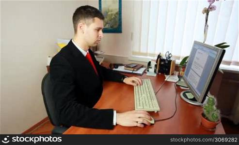 handsome young man in suit with red tie, begins typing some documents
