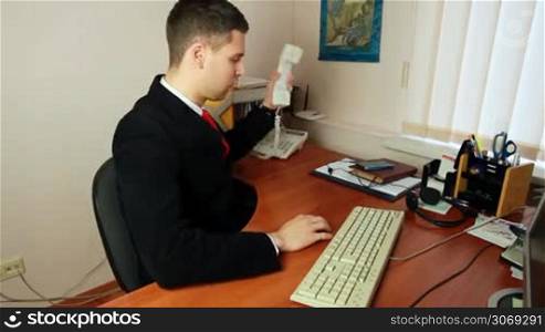 handsome young man in suit with red tie, talking on phone and taking notes at work, closeup