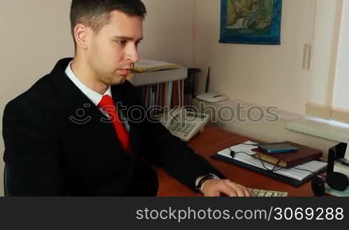 handsome young man in suit with red tie, talking on phone at work, closeup