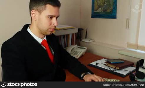 handsome young man in suit with red tie, talking on phone at work, closeup