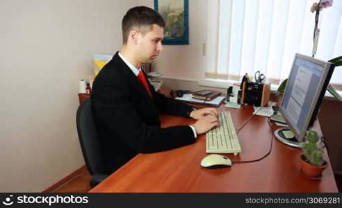 handsome young man in suit with red tie, typing some documents at work