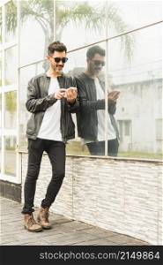 handsome young man leaning glass wall using smartphone