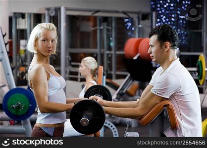 Handsome young man lifting weights assisted by a female trainer