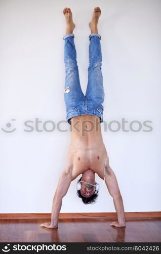 handsome young man listening music on headphones at modern home over white wall and standing on hands