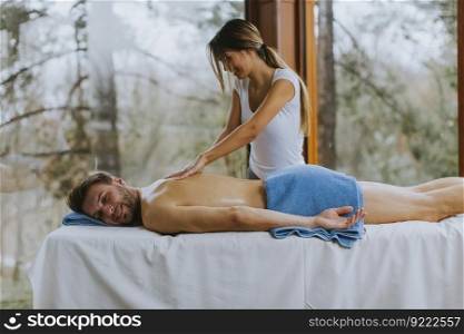 Handsome young man lying and having back massage in spa salon during winter season by the female masseur